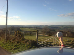 Photograph of someone holding a MikroTik SXT out of a car window, aimed towards the distant hills.